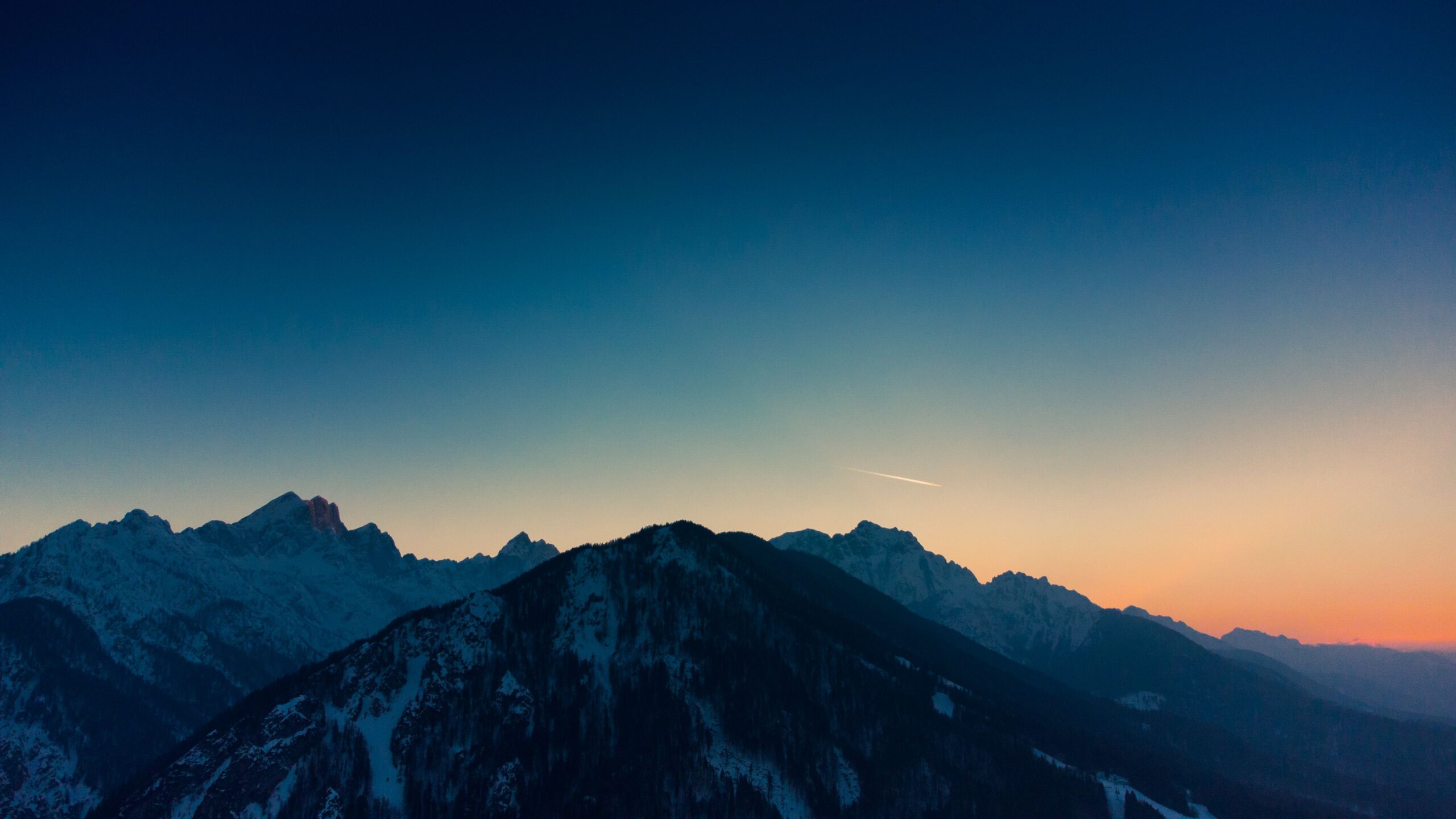 A breathtaking view of snow-capped mountains during twilight with a clear sky.